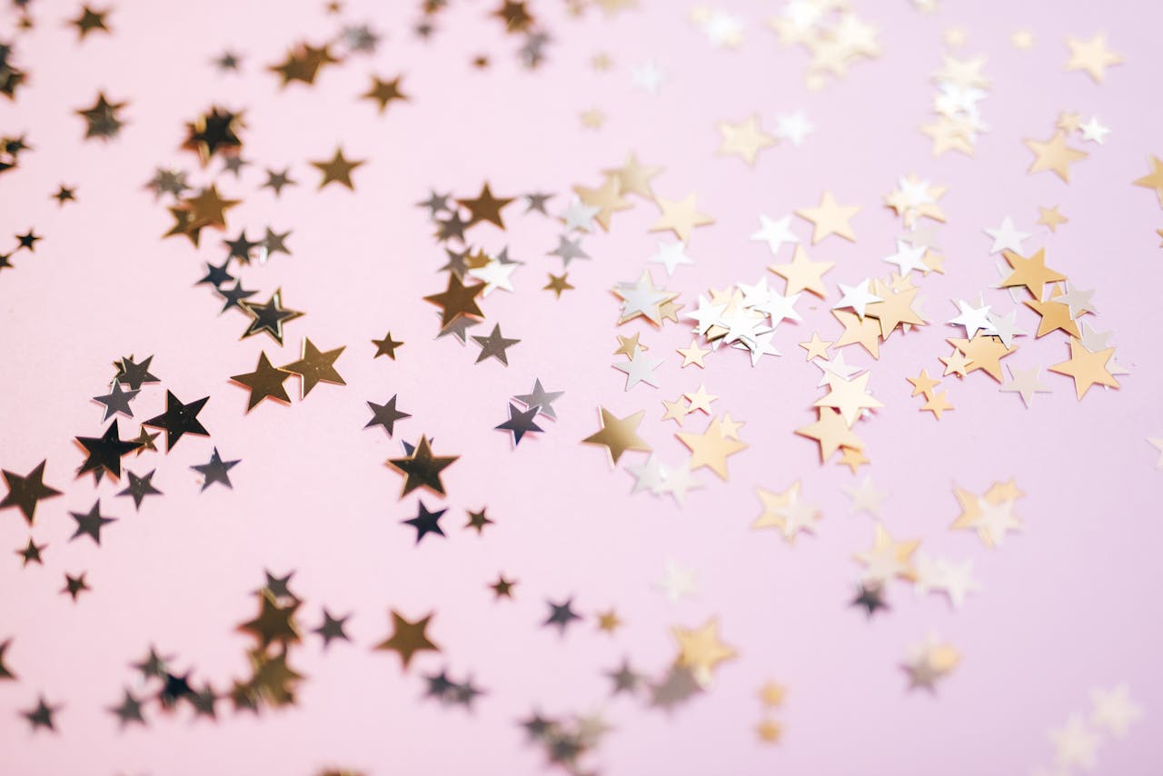 our-services-3 Gold and silver star confetti spread across a pastel pink surface, creating a festive and whimsical effect.
