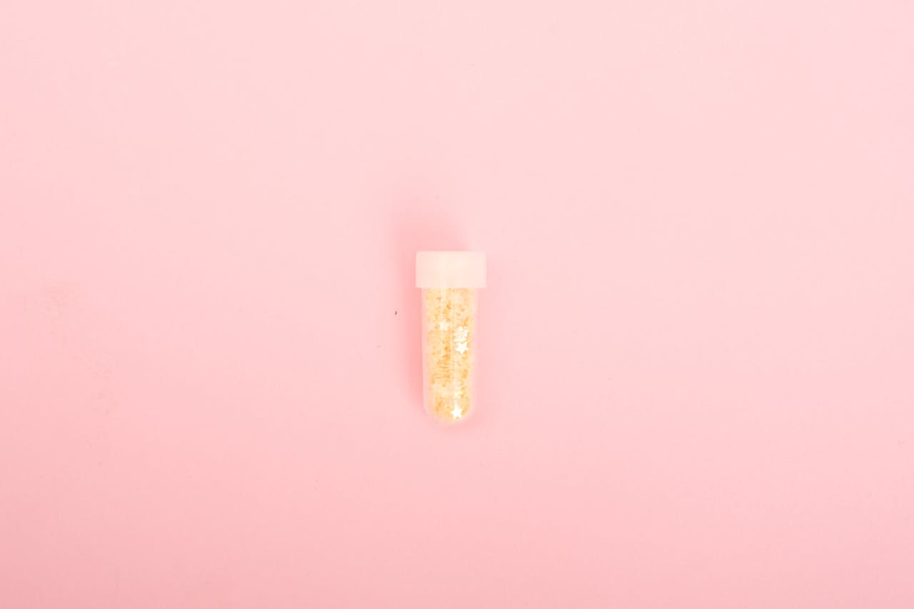 A small tube of golden glitter on a bright pink background, perfect for creative projects.